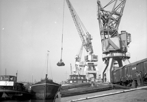 854050 Afbeelding van de overslag van goederen van schip naar spoor op een kade in de haven van Rotterdam.